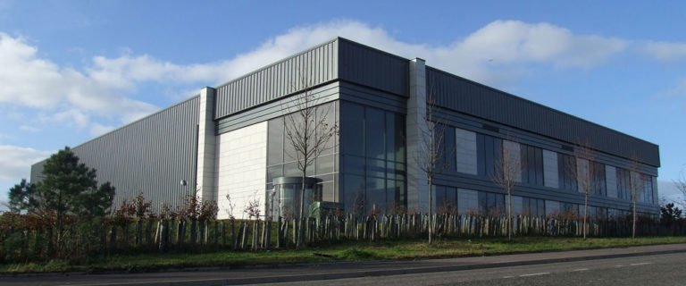 Mackie Ramsay Taylor — Large modern industrial building with reflective windows under a clear blue sky