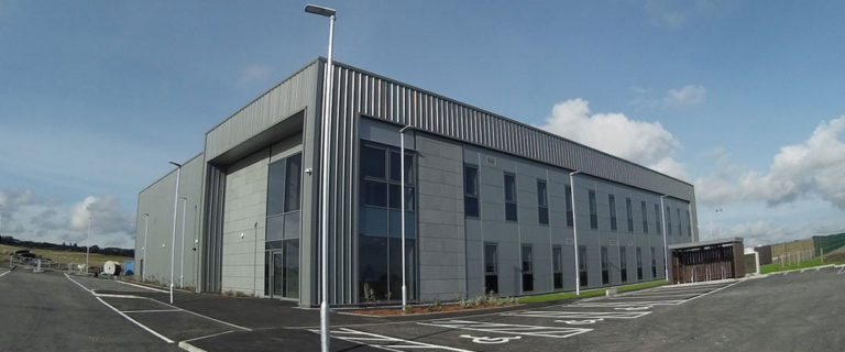 Mackie Ramsay Taylor — Modern two-story industrial building with parking lot under a cloudy sky