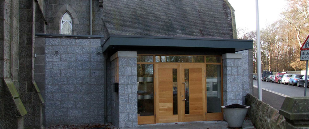 Modern wooden doors on a stone building with a street and parked cars in the background