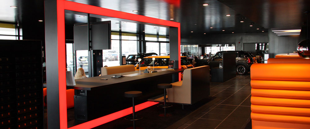 A modern car showroom with a red and black interior, desks for customers, and cars on display